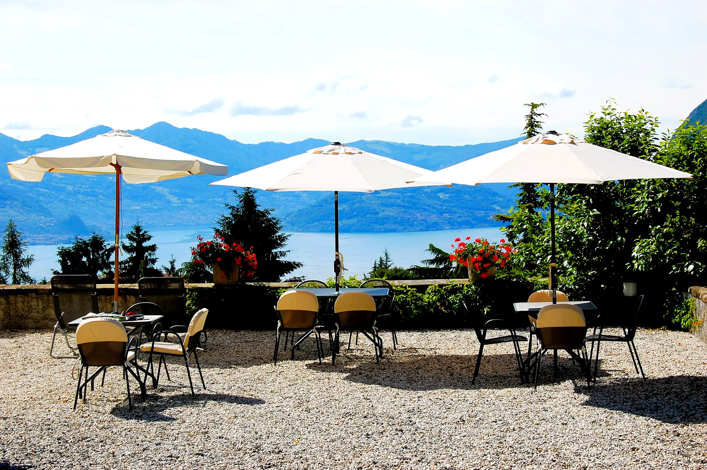 The sun terrace with three parasols, the tables and Lake Iseo between the mountains